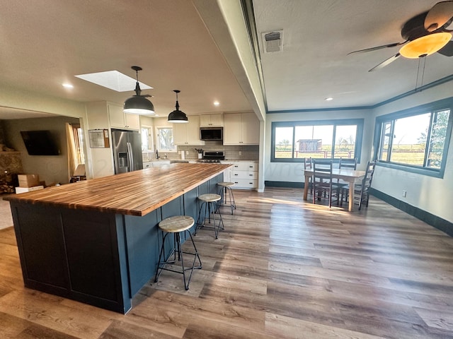 kitchen with white cabinets, hanging light fixtures, light hardwood / wood-style flooring, and appliances with stainless steel finishes