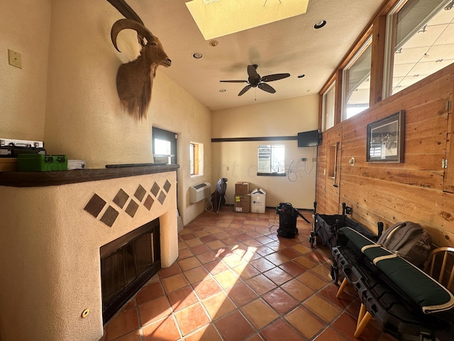 tiled living room with a wall unit AC, a wealth of natural light, wood walls, and ceiling fan