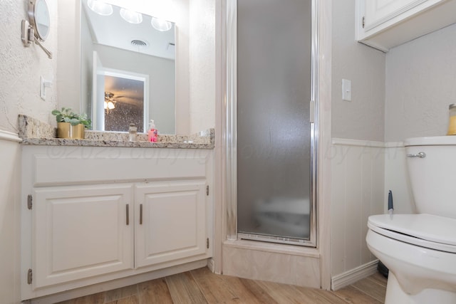 full bath with a shower stall, toilet, wood finished floors, a wainscoted wall, and a textured wall