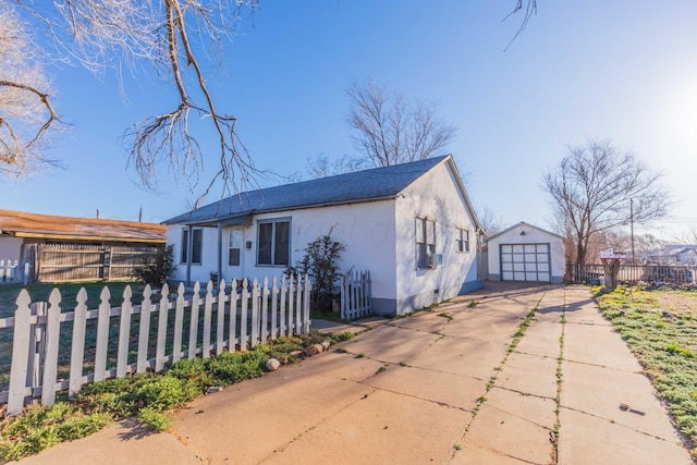 bungalow-style house featuring a fenced front yard, a garage, an outdoor structure, concrete driveway, and stucco siding