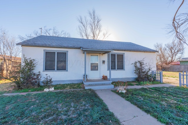 bungalow-style home with roof with shingles, fence, a front lawn, and stucco siding