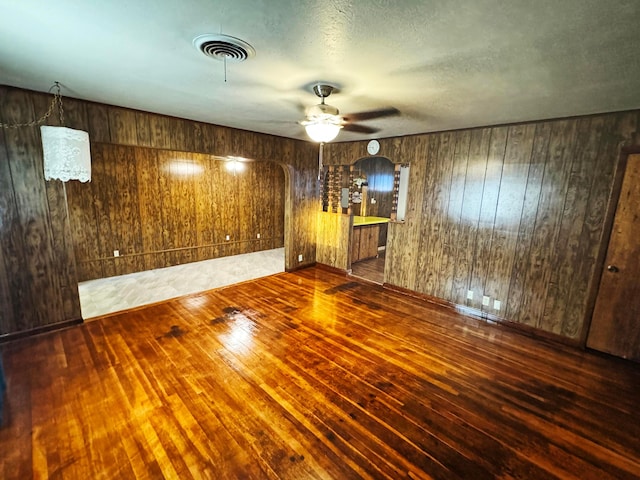 unfurnished room with ceiling fan, wooden walls, and dark hardwood / wood-style flooring