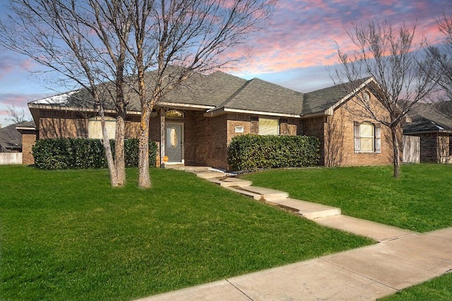 ranch-style home featuring roof with shingles, a front lawn, and brick siding