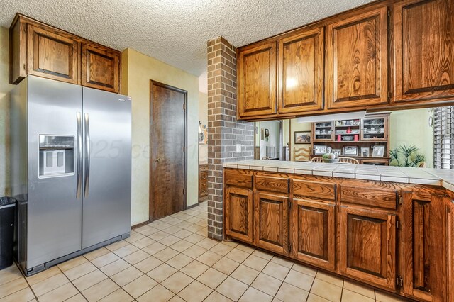 300 W 11th St, Wheeler, TX 79096 - kitchen with stainless steel fridge with ice dispenser, brown cabinetry, light tile patterned flooring, a textured ceiling, and tile counters