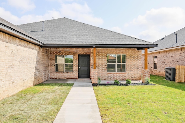 entrance to property featuring central air condition unit, brick siding, a yard, and a shingled roof