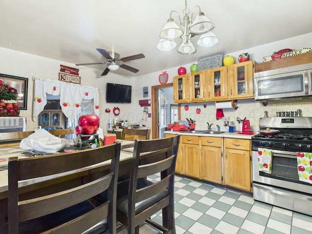 kitchen with light countertops, a sink, light floors, appliances with stainless steel finishes, and ceiling fan with notable chandelier