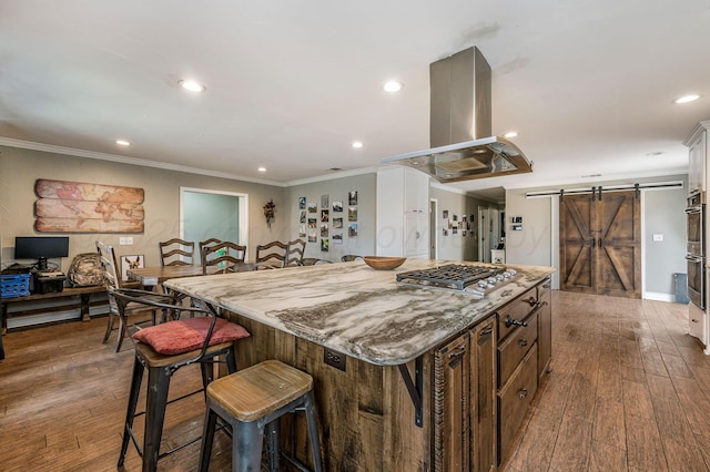 kitchen with island range hood, appliances with stainless steel finishes, a kitchen breakfast bar, a kitchen island, and a barn door