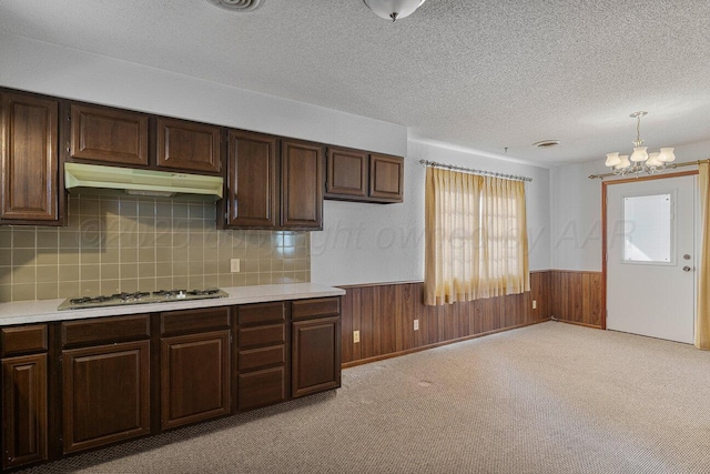 kitchen featuring a wainscoted wall, under cabinet range hood, wooden walls, light countertops, and white gas stovetop