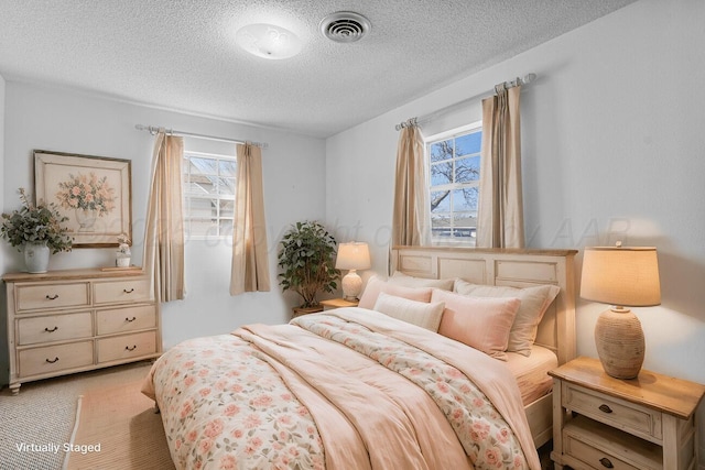 bedroom featuring visible vents, light colored carpet, and a textured ceiling