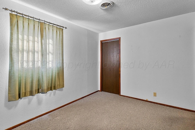 carpeted spare room with visible vents, baseboards, and a textured ceiling