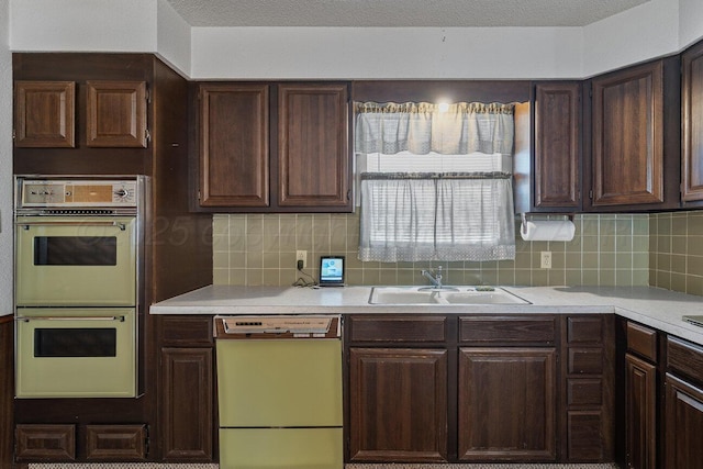 kitchen with dishwashing machine, double wall oven, light countertops, and a sink