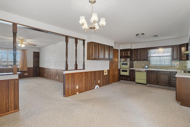 kitchen with a textured ceiling, wood walls, wainscoting, light countertops, and dishwasher