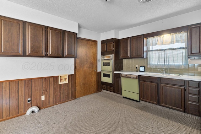 kitchen with double wall oven, a sink, light countertops, wood walls, and dishwasher