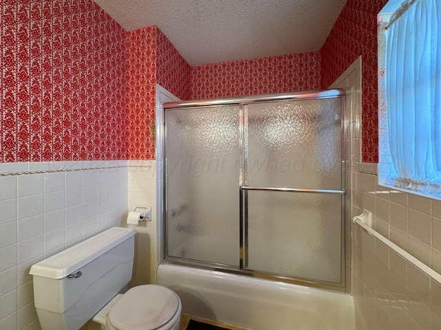 bathroom with a wainscoted wall, wallpapered walls, a textured ceiling, tile walls, and toilet