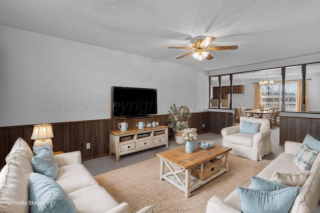 carpeted living room with ceiling fan with notable chandelier, wainscoting, a textured ceiling, and wood walls