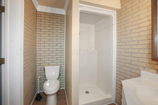 bathroom with brick wall, ornamental molding, vanity, walk in shower, and toilet