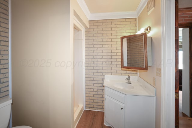 bathroom featuring toilet, wood-type flooring, ornamental molding, vanity, and brick wall