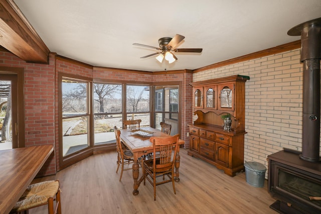 dining area featuring ceiling fan, brick wall, a wood stove, and light wood-type flooring