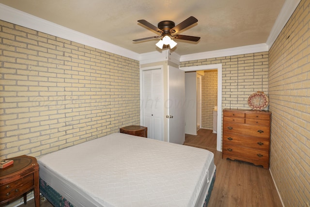 bedroom with wood-type flooring, brick wall, crown molding, and a closet