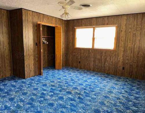 1035 N Duncan St, Pampa, TX 79065 - unfurnished bedroom featuring carpet, wood walls, ceiling fan, and a closet