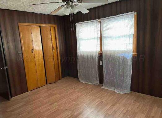1035 N Duncan St, Pampa, TX 79065 - unfurnished bedroom with light wood finished floors, a closet, a ceiling fan, and wood walls
