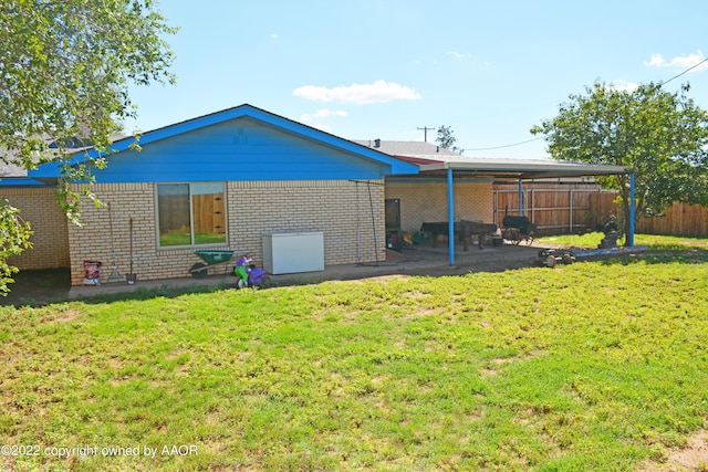 back of property featuring an attached carport, brick siding, fence, and a yard