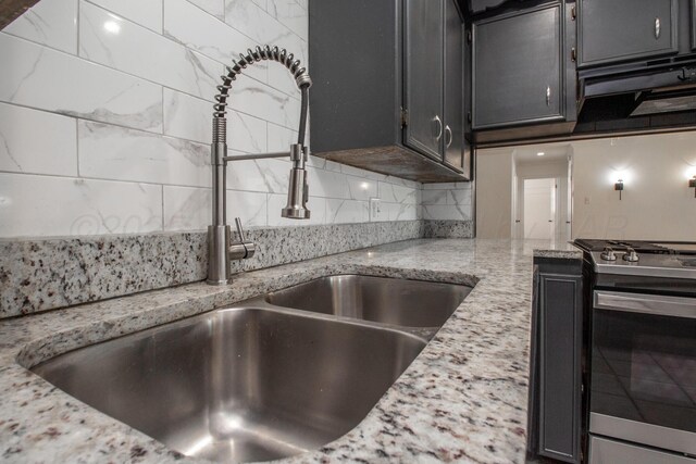 4808 SW 57th Ave, Amarillo, TX 79109 - kitchen featuring stainless steel gas range oven, under cabinet range hood, decorative backsplash, light stone counters, and dark cabinets