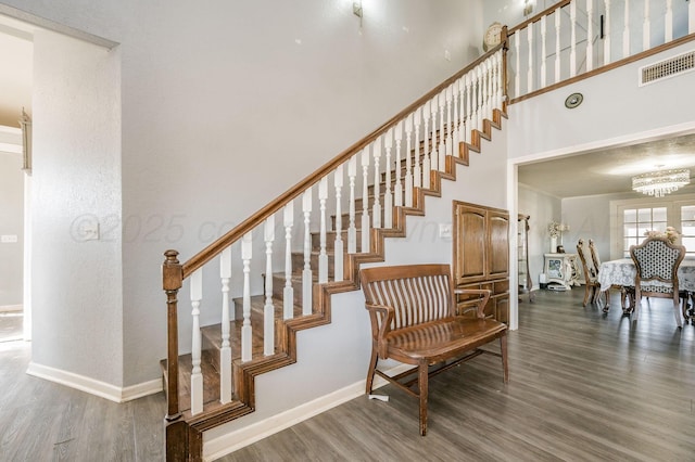 stairs with a towering ceiling, baseboards, visible vents, and wood finished floors