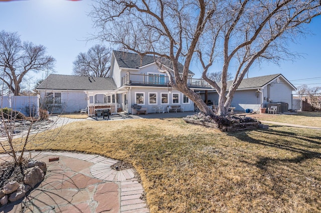 rear view of property with a balcony, fence, a lawn, and a patio