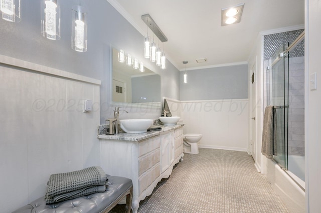 bathroom with crown molding, double vanity, toilet, combined bath / shower with glass door, and a sink