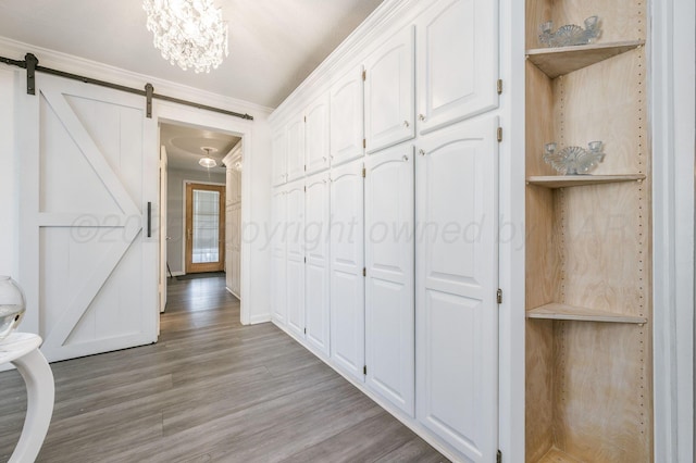 hallway with ornamental molding, a barn door, light wood-type flooring, and an inviting chandelier