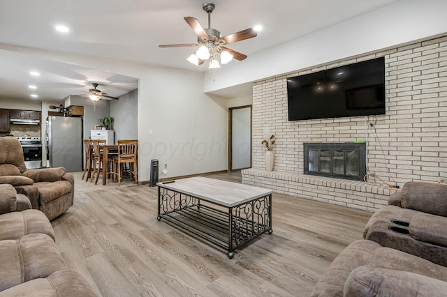 living room with ceiling fan, light wood-type flooring, a brick fireplace, and lofted ceiling