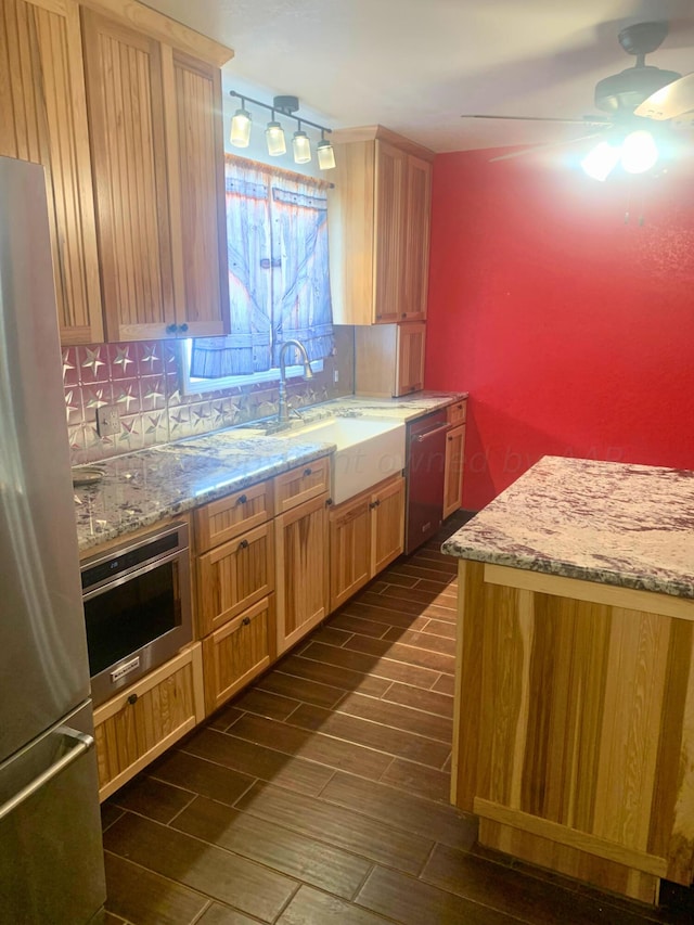 kitchen with sink, tasteful backsplash, light stone counters, appliances with stainless steel finishes, and ceiling fan