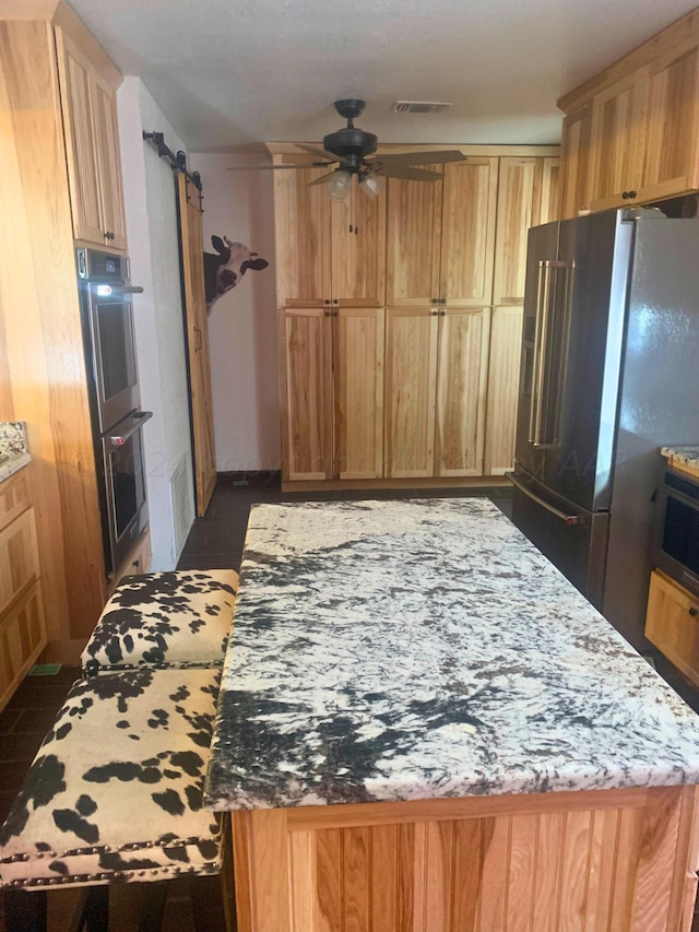 kitchen featuring ceiling fan, stainless steel appliances, a barn door, and light stone countertops