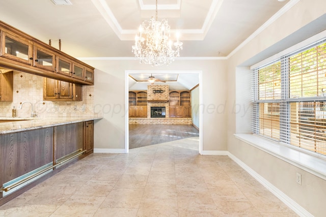 kitchen with light stone counters, decorative backsplash, ornamental molding, a fireplace, and decorative light fixtures