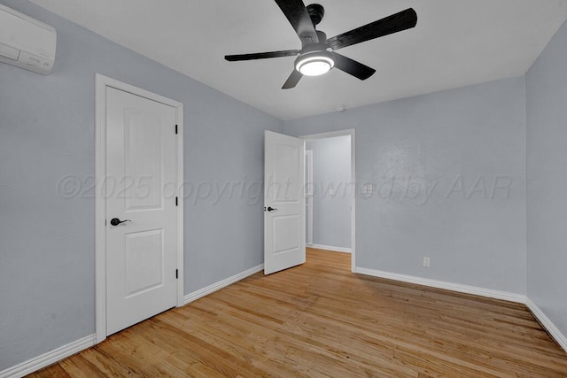 unfurnished bedroom with an AC wall unit, baseboards, ceiling fan, and light wood-style floors