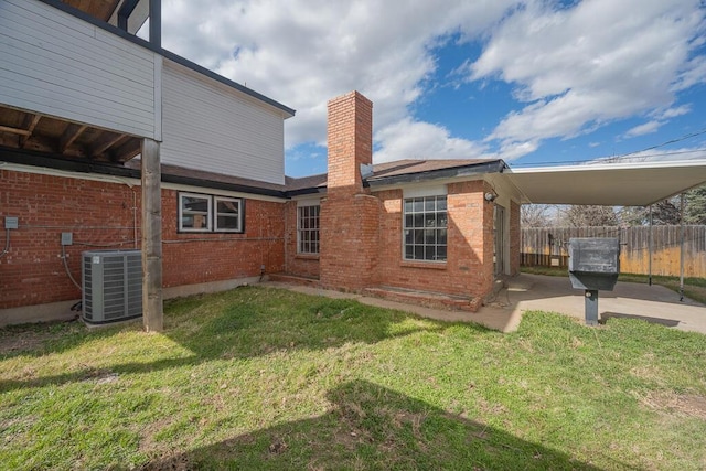 rear view of property with a patio, brick siding, central AC unit, fence, and a lawn