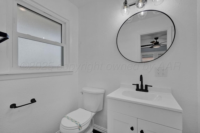 half bathroom with toilet, ceiling fan, vanity, and baseboards
