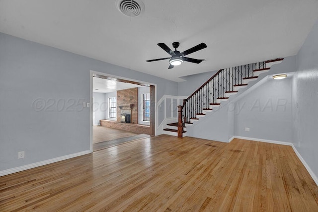 unfurnished living room featuring wood finished floors, a brick fireplace, visible vents, and stairs