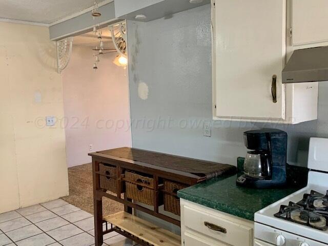 kitchen with white cabinets, white gas range, light tile patterned floors, and range hood