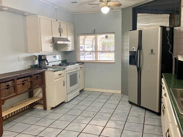 kitchen featuring stainless steel fridge, light tile patterned floors, white cabinets, gas range gas stove, and ceiling fan