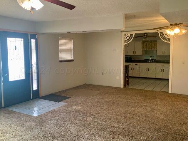 unfurnished living room featuring sink, light colored carpet, and ceiling fan