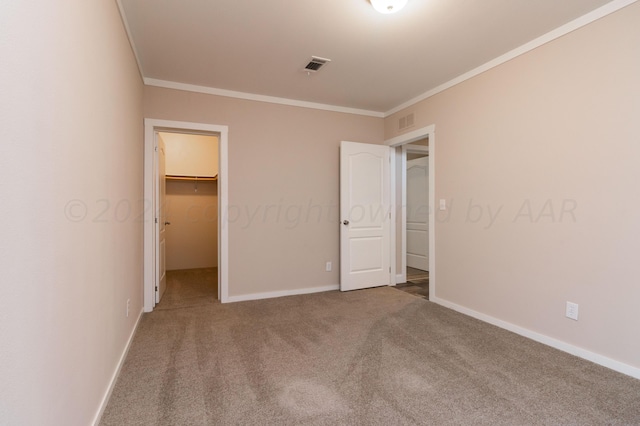 unfurnished bedroom featuring carpet flooring, a closet, a walk in closet, and ornamental molding