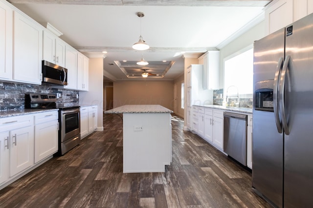 kitchen with light stone counters, stainless steel appliances, decorative light fixtures, white cabinets, and a center island