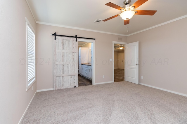 unfurnished bedroom featuring a barn door, crown molding, dark carpet, and connected bathroom