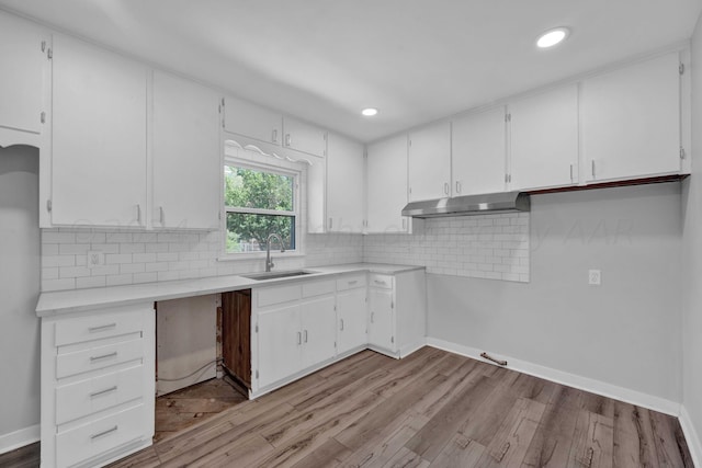 kitchen with under cabinet range hood, white cabinetry, light countertops, and a sink