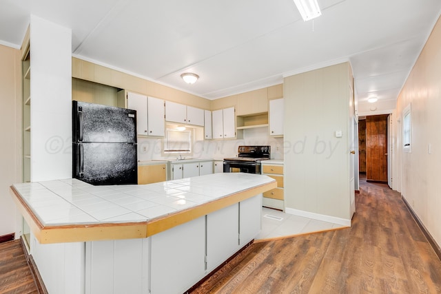 kitchen featuring tile counters, light wood finished floors, black appliances, and a peninsula