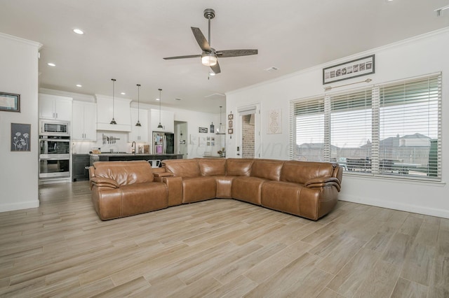 living area featuring ornamental molding, baseboards, ceiling fan, and light wood finished floors