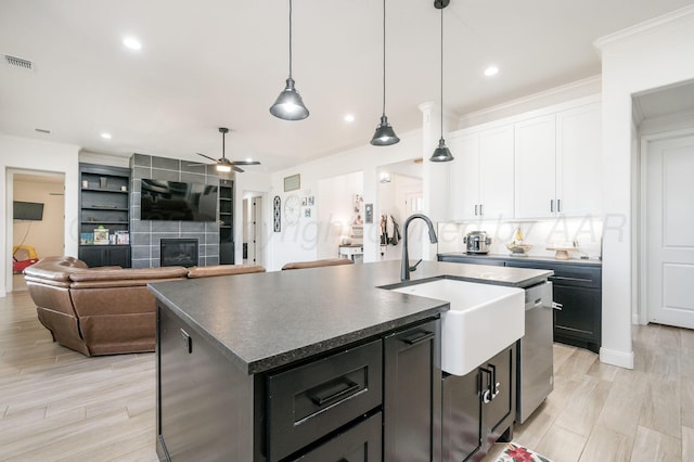 kitchen featuring decorative light fixtures, dark countertops, white cabinetry, an island with sink, and dishwasher