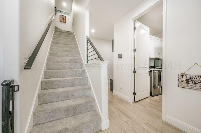 staircase featuring baseboards, washer / clothes dryer, wood finished floors, and recessed lighting